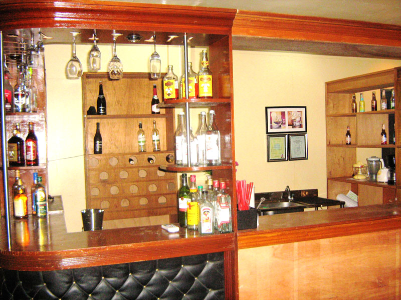 A bar counter with bottles, glassware and stools