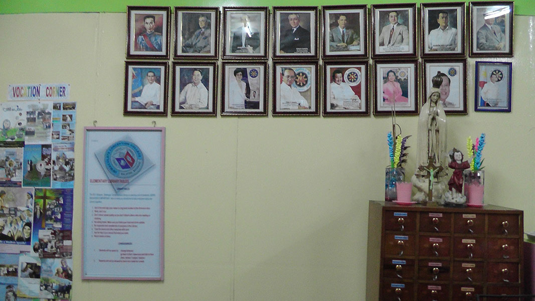 Rows of framed portraits above a card catalog cabinet and a statue of Mary