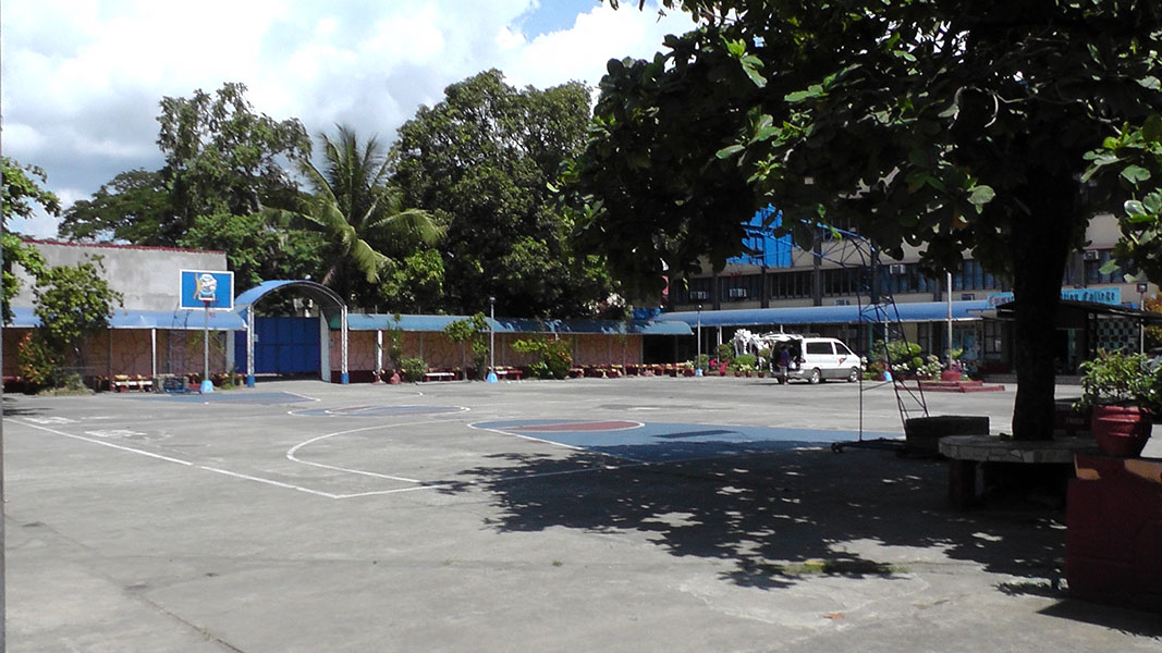 An open court ringed by trees and blue-painted school buildings